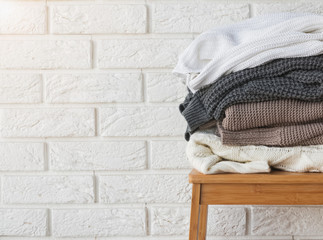 Stack of winter sweaters on the white brick wall background.