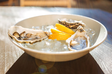 Standing on table. Fresh tasty oysters and lemon slices standing on the table on sunny summer terrace