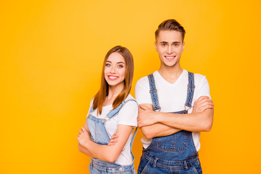 Portrait of happy lovely cheerful adorable young cute couple with folded arms, girl standing back to guy, looking straight over yellow background, isolated, copy space