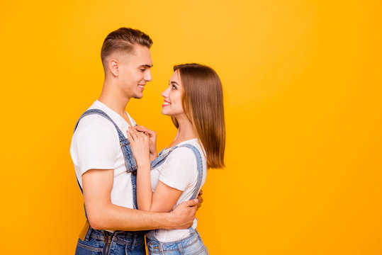 Portrait of cheerful cute young couple in love, wearing casual, hugging, looking at each other, smiling over yellow background, isolated, copy space