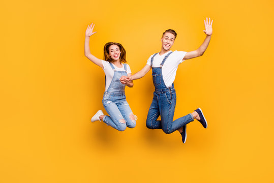 Full length portrait of beautiful attractive playful cheerful, comic couple wearing casual outfit, jeans, shirts jumping in the air on yellow background showing highfive