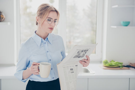 Young attractive cute adorable woman office worker wearing spectacles keeping and reading newspaper early in the morning and having a drink in kitchen