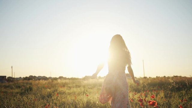 Gorgeous Ukrainian beauty running through field full of red flowers. Attractive Caucasian girl in pink dress in the evening. Countryside. Summertime. Sunset. Outdoors.