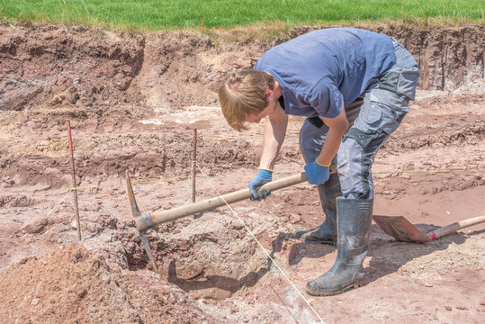 Mann hebt Fundamente aus mit Spitzhacke