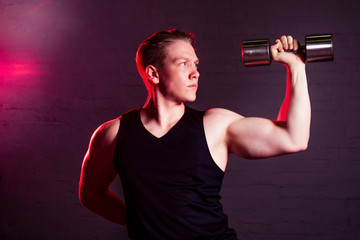 Fototapeta na wymiar young handsome white man in black t-shirt is engaged with dumbbells in a gym on a black brick background