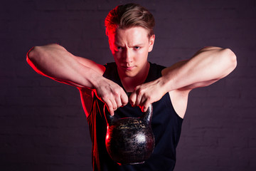 young handsome white man in black t-shirt engaged with a kettlebell in the gym on a black brick background