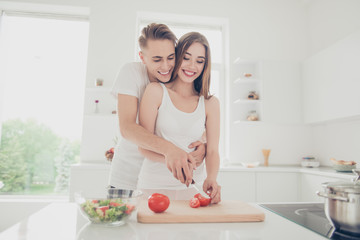 Fototapeta na wymiar Portrait of young attractive cute lovely couple together in kitchen, wearing pajama, cooking food, salad, chopping vegatables