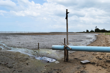 Dirty water flows through the blue PVC pipe into the sea , The beach is sandy and muddy
