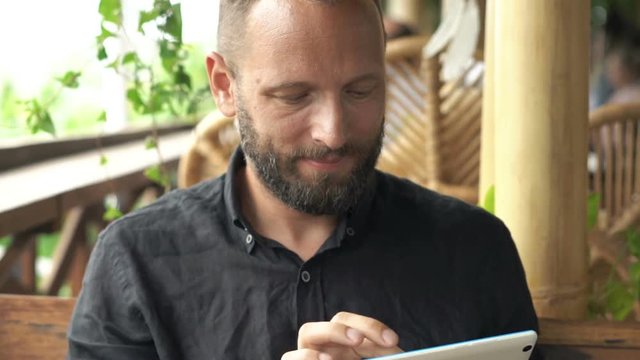 Young, happy man surfing Internet on tablet sitting in cafe
