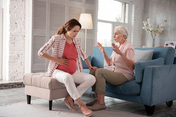 Calming daughter. Caring concerned mother calming her pregnant daughter having severe ache in belly