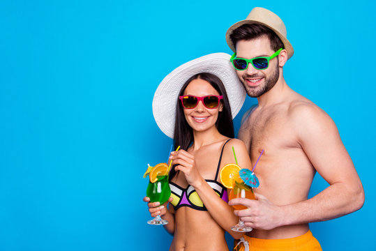 Handsome guy on a date with a beard hug attractive young model in wide brim hat hold cocktails in hand isolated on blue background with copy space for text