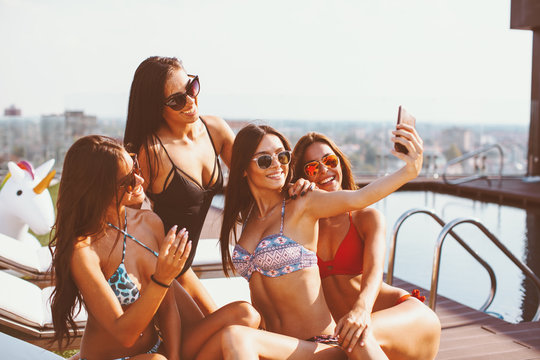 Four young women in a penthouse near the pool doing selfie in a bikini