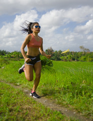 attractive and very fit Asian sport woman training running workout at green field landscape background working hard in healthy lifestyle