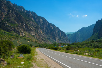 Fototapeta premium Mountain landscape, Elbrus region, Kabardino-Balkaria. In the foreground, an asphalt winding road with road markings on the background of mountains and blue sky