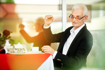 Old gray-haired bussines man sit at the restaurant and call the waiter