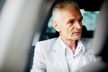 Old bussines man sitting in the car and look around. Thinking about new possibilities.