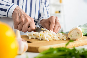 Obraz na płótnie Canvas cropped image of grey hair woman cutting leek on wooden board in kitchen