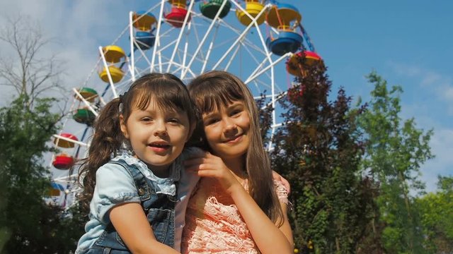 Portrait of happy children in amusement park. Sisters hugging in the park.