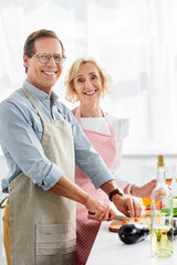 smiling husband cutting vegetables on wooden board in kitchen and looking at camera