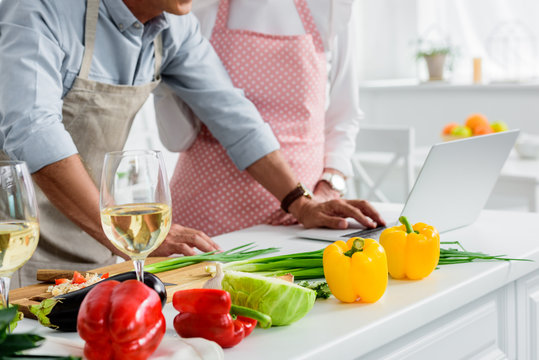 cropped image of senior couple cooking at kitchen and using laptop - Powered by Adobe