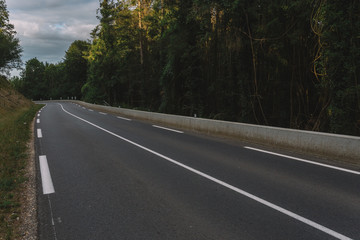 Empty asphalt country road passing through green forests and villages. Summer countryside landscape in the region of Normandy, France. Recreation, nature, holidays, travel and road network concept.