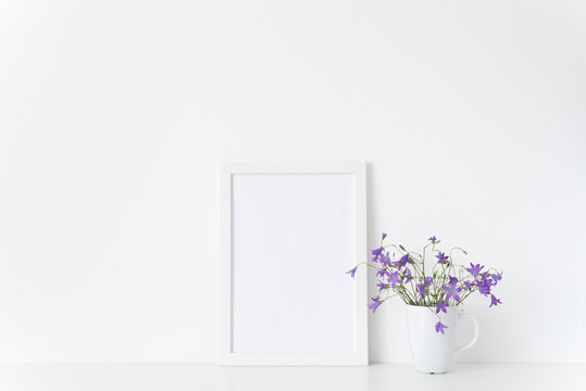 Minimal white portrait a4 frame mockup with wild lilac flowers in mug near white wall. Empty frame mock up for presentation design. Template framing for modern art.