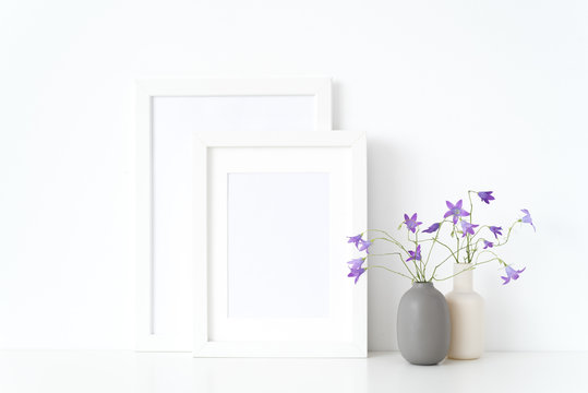 White portrait a4, a5 frame mockup with wild sprihg bellflowers in vases near wall on white background. Empty frame mock up for presentation design. Template framing for modern stylish art.