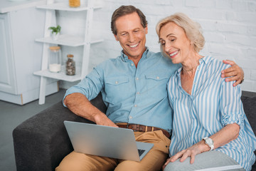 smiling senior couple using laptop while sitting together at home