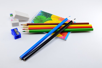 Fototapeta premium Colorful pencils with erasers, sharpener and note pad on white background.