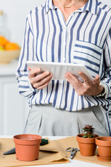 cropped shot of senior woman using digital tablet while cultivating plants at home