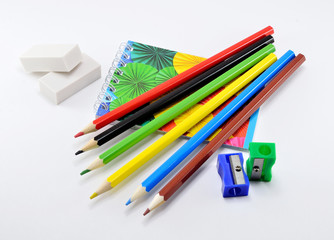 Colorful pencils with erasers, sharpener and note pad on white background.