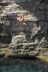 Obraz premium Frau im Bikini klettert an Felswand über dem Wasser