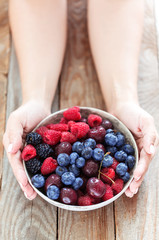 Holding clay bowl filled with fresh juicy berries.