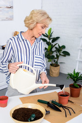 beautiful senior woman watering soil with watering can at home