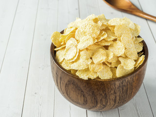 Dry corn flakes in wooden bowl on light background