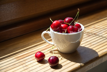 Cherry berries in a white cup on a wooden background with a light from the window