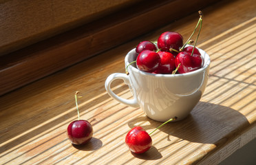 Cherry berries in a white cup on a wooden background with a light from the window