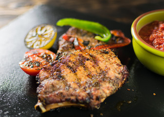 Grilled meat served with vegetables, spices on a slate plate.