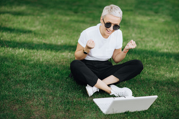 Fototapeta premium Attractive trendy happy hipster young woman with notebook in hat and sunglasses have fun in the park on the grass.