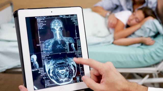 Close up doctor checking MRI results on tablet PC with teen patient girl sleeping on hospital bed in the background