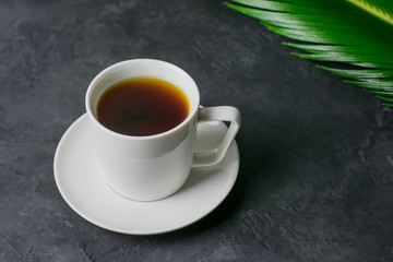 A cup of tea and a palm leaf on a dark background