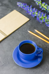 Opened sketchbook, blue cup, pencils and blue flowers on the table