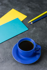 A blue cup, colored envelopes (blue and yellow) and pencils on a dark table