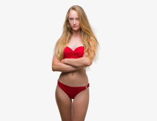 Blonde teenager woman wearing red bikini skeptic and nervous, disapproving expression on face with crossed arms. Negative person.
