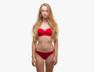 Obraz premium Blonde teenager woman wearing red bikini with serious expression on face. Simple and natural looking at the camera.