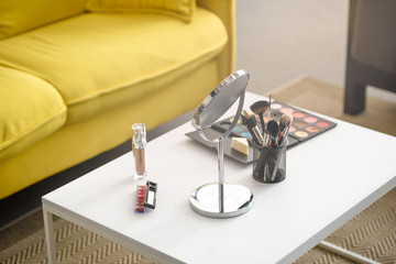close up view of yellow sofa, mirror, makeup brushes and cosmetics on coffee table