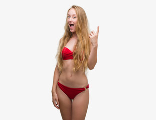 Blonde teenager woman wearing red bikini pointing finger up with successful idea. Exited and happy. Number one.
