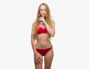 Blonde teenager woman wearing red bikini asking to be quiet with finger on lips. Silence and secret concept.