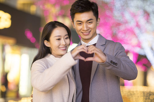 Cheerful young Chinese couple making heart shape with their hands