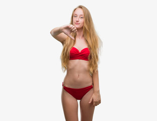 Blonde teenager woman wearing red bikini looking unhappy and angry showing rejection and negative with thumbs down gesture. Bad expression.